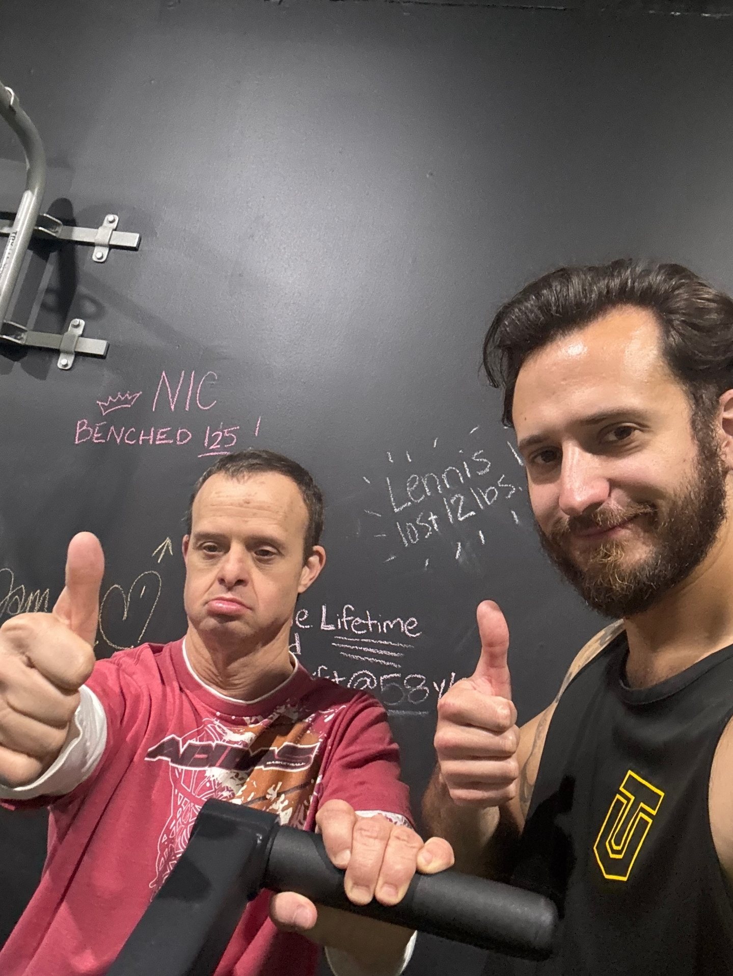 Garret and an athlete giving a thumbs up in front of the gym chalkboard