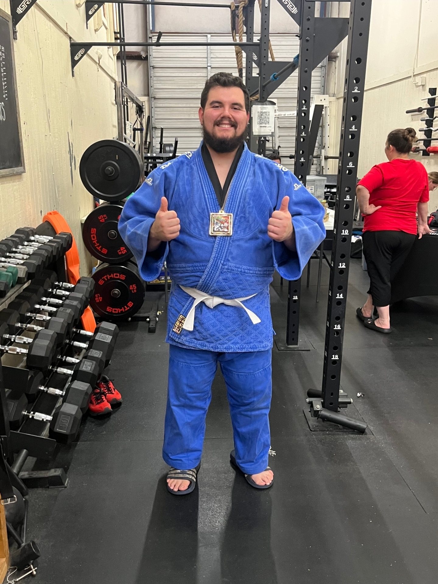 Jessie in a blue judo gi with a medal around his neck, two thumbs up