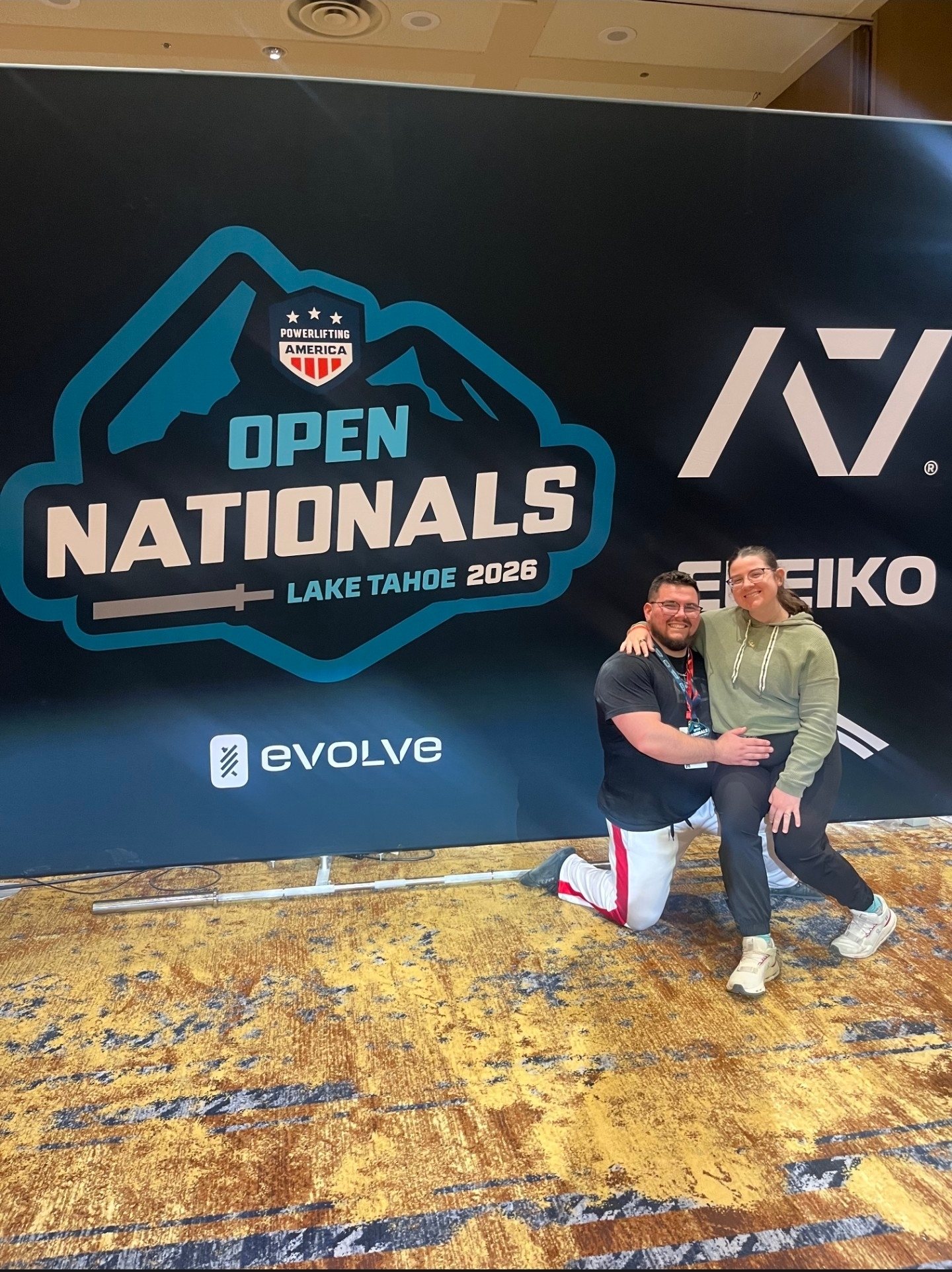 Jessie on one knee with Emily beside him in front of the Open Nationals 2026 banner in Lake Tahoe