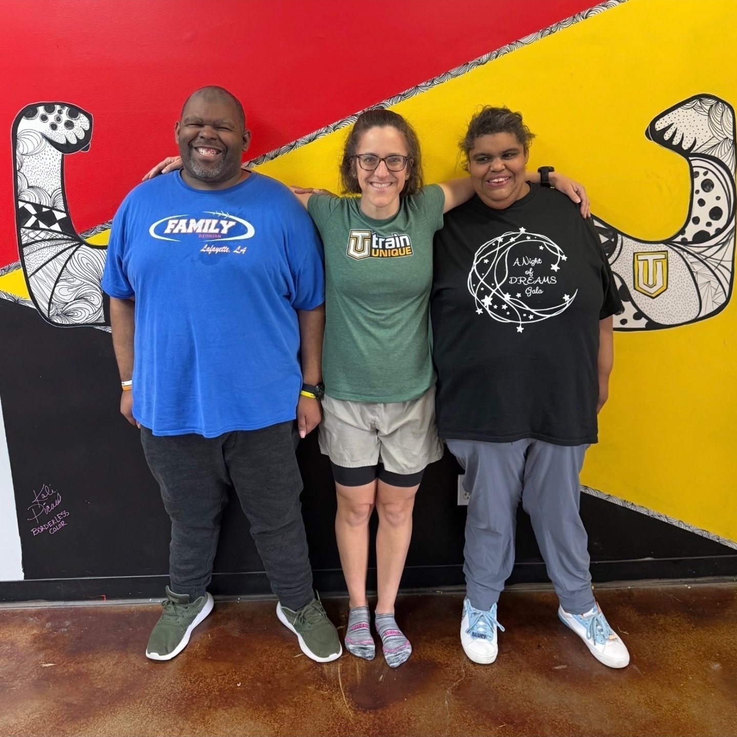 Elizabeth with two of her athletes in front of the flexing-arms mural at the Lafayette gym
