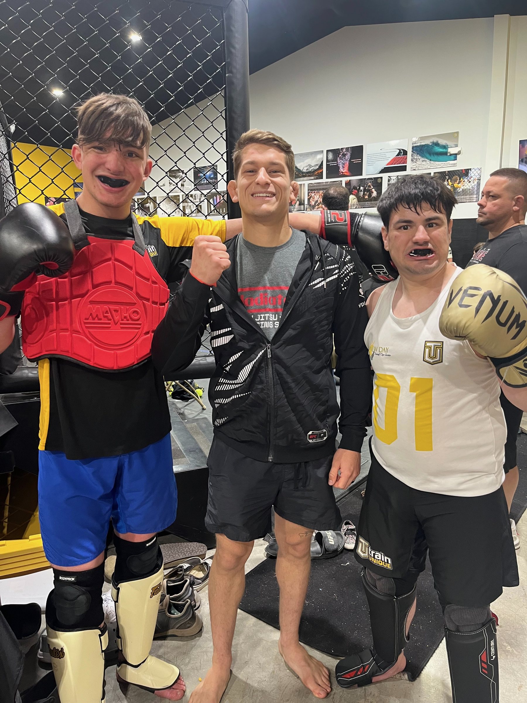 Two athletes in their gear with their coach in front of the cage
