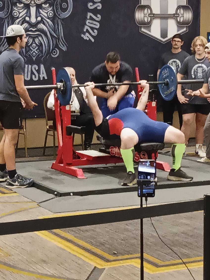 A Train Unique lifter benching on the platform with a spotter over the bar