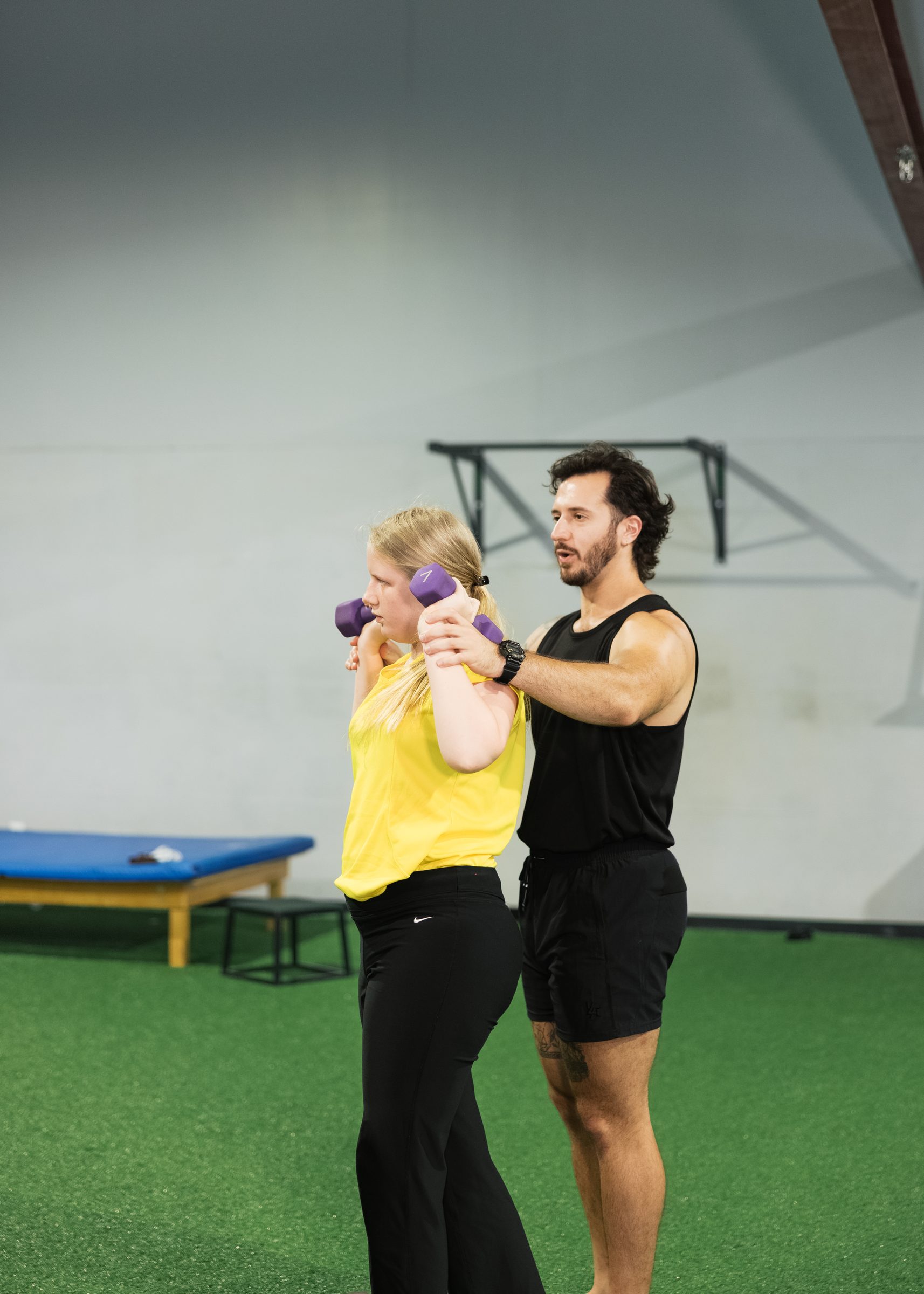 A coach guiding an athlete through a dumbbell press