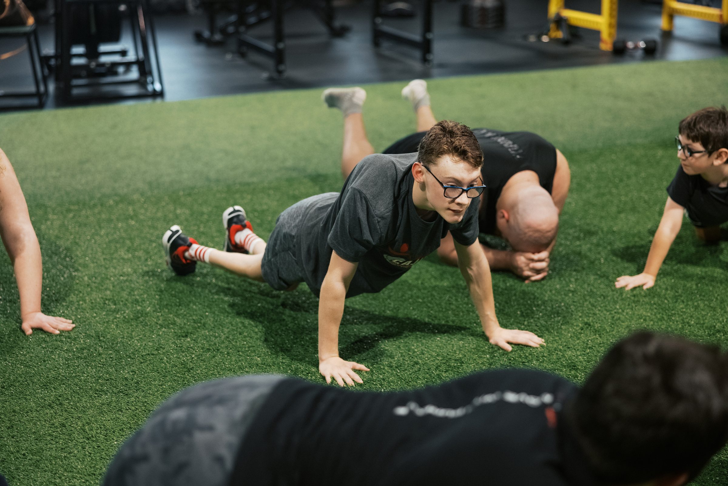 An athlete driving low across the turf, coach beside him