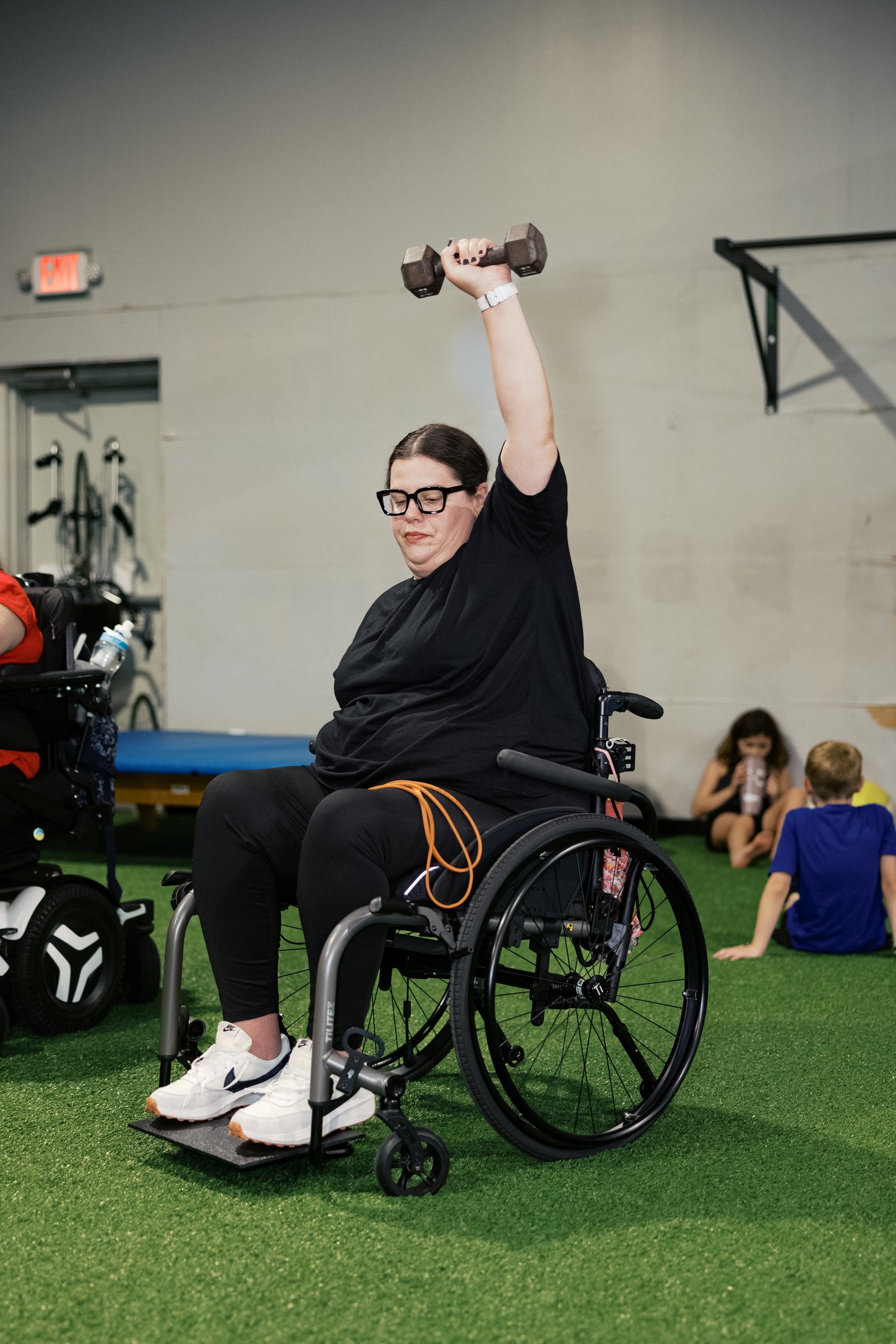 An athlete pressing a dumbbell overhead from her wheelchair